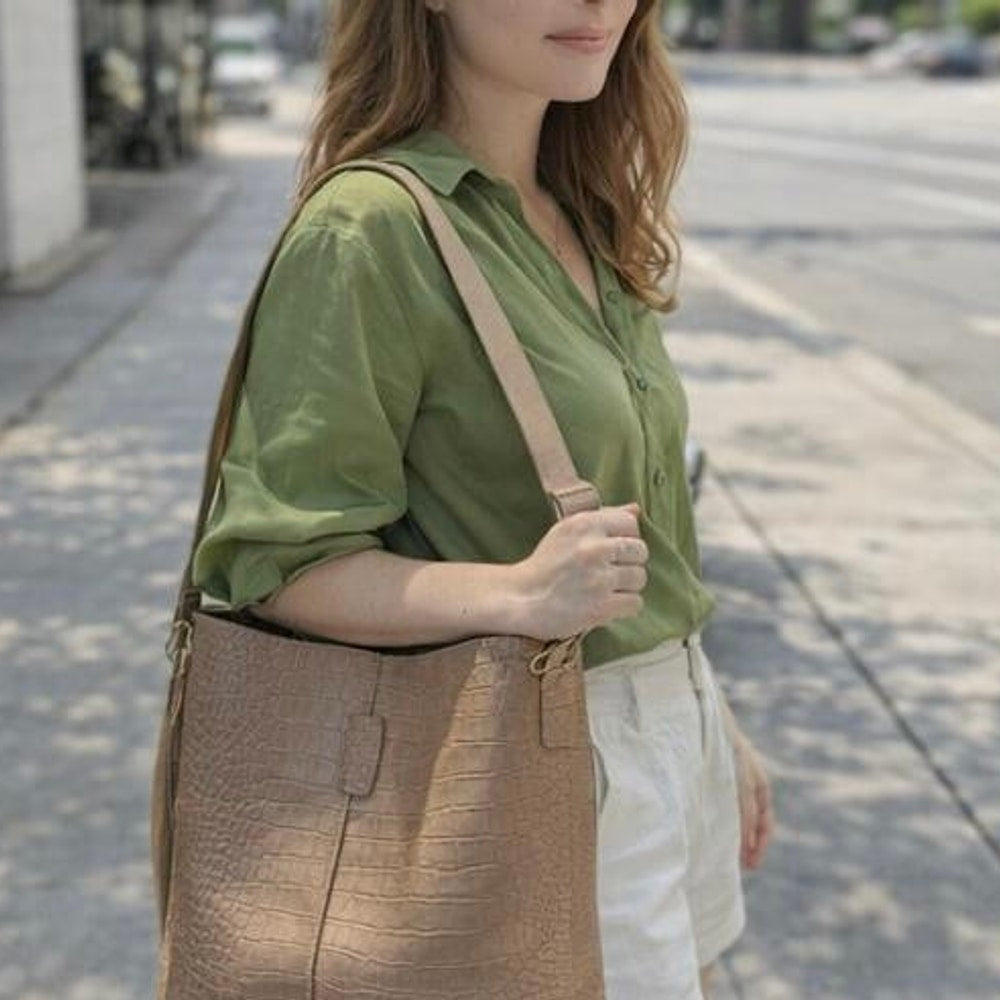 Woman wearing a green shirt and brown skirt with a beige bag on a city street.