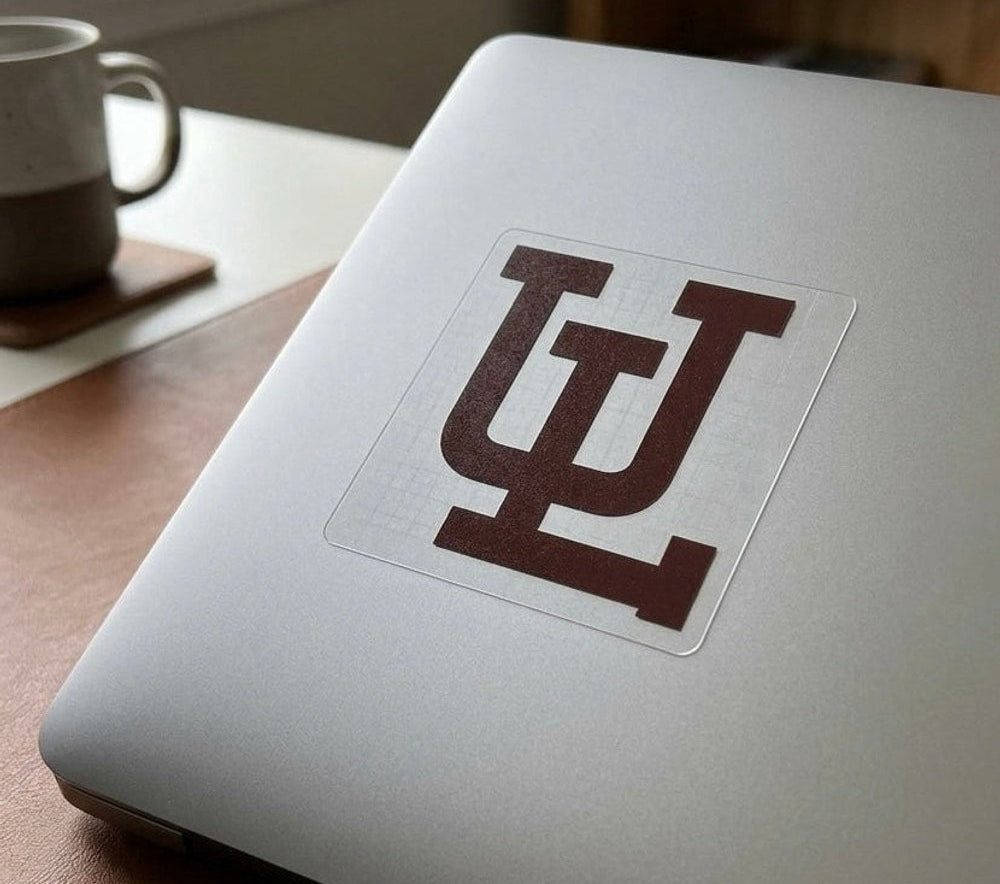 Laptop with a brown Union de Laguna logo on a wooden surface next to a mug.