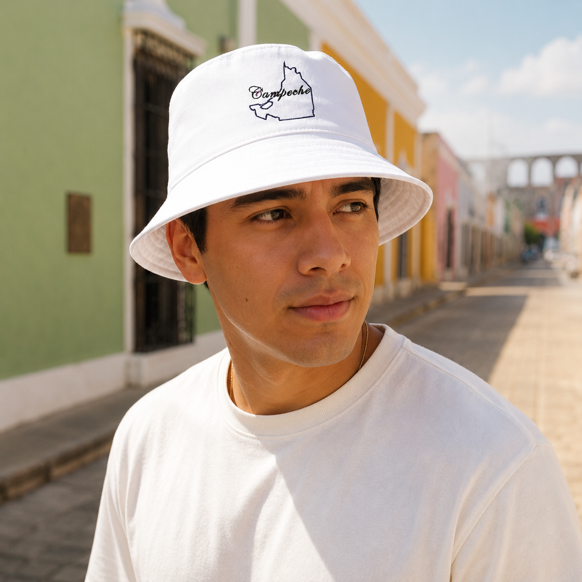 A Mexican model wearing the Campeche bucket hat in a realistic outdoor lifestyle setting, with the front design clearly visible. The Campeche bucket hat design, shape, and colors are shown clearly in a natural casual scene.