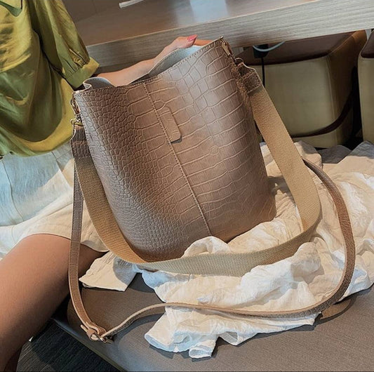 A brown croc crossbody bag with a hasp closure and a strap, placed on a table.
