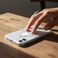 Hand pressing a die-cut bubble-free sticker of Mexico’s silhouette with black text reading “Mexico City” onto a silver smartphone — featuring a clean white design with black outline, symbolizing national pride and minimalist style.