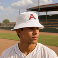 A man wearing a white baseball bucket hat with a red and white 'A' logo for Acereros, standing on a baseball field.