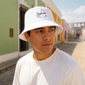 A Mexican model wearing the Campeche bucket hat in a realistic outdoor lifestyle setting, with the front design clearly visible. The Campeche bucket hat design, shape, and colors are shown clearly in a natural casual scene.