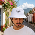 A Mexican model wearing the Chiapas bucket hat in a realistic outdoor lifestyle setting, with the front design clearly visible. The Chiapas bucket hat design, shape, and colors are shown clearly in a natural casual scene.
