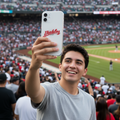 A man in a gray t-shirt takes a selfie in a crowded baseball stadium, holding a white phone with a red 'Dialos' logo on the back.