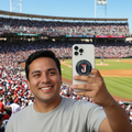 A man taking a selfie in a crowded baseball stadium, holding a white phone on a "Toros de Tijuana" case.