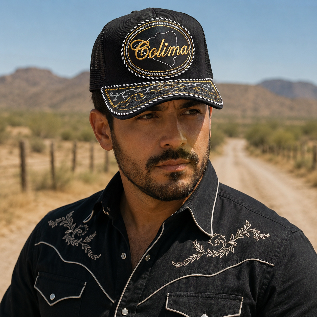 A Mexican model wearing a black Coahuila charro-style hat on a desert ranch road with mountains in the background. The embroidered Coahuila name and map design are clearly visible on the front.