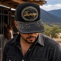 A Mexican model wearing a black Durango charro-style hat near a rustic stable and mountain landscape. The embroidered Durango name and map design are clearly visible on the front.