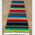 Long multicolor rainbow striped table runner with narrow bands and white fringe at one end.