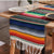 Multicolor striped table runner with dark blue top bands and white fringe along the edge.
