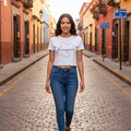 A woman walking down a cobblestone street wearing a white graphic t-shirt with a black outline of Guatemal and the word 'Guatemalteca' across the chest, paired with blue jeans.