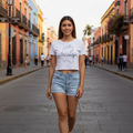 A woman wearing a white crop t-shirt with the text 'Hidalgo' printed in black on the front, paired with blue jeans.