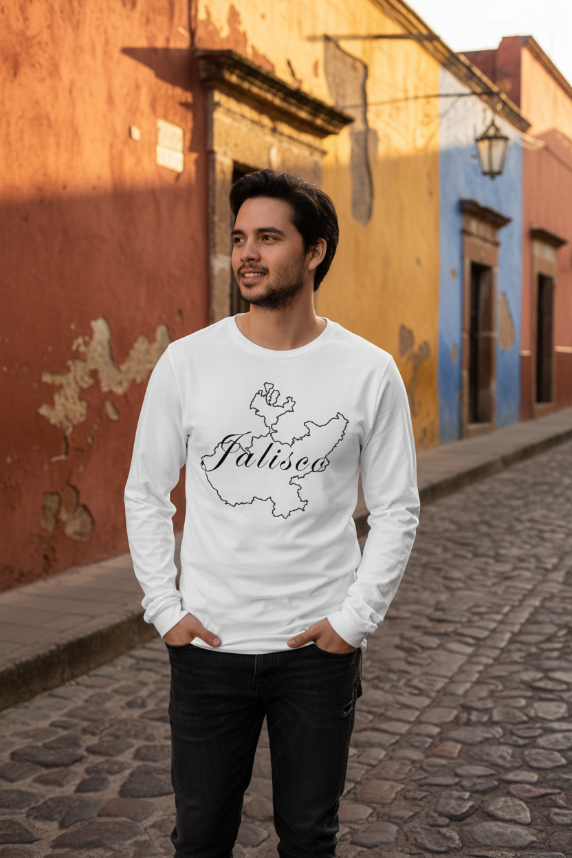 A man wearing a white long-sleeve t-shirt with a black map outline and the word 'Jalisco' printed on the front, standing on a cobblestone street in front of colorful buildings.