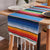Blue rainbow striped table runner with multicolor bands and white fringe trim on the edges.