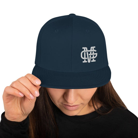 A person wearing a Mariachis de Guadalajara dark navy snapback hat with an embroidered Mariahis de Guadalajara logo on the front.