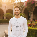 A man wearing a white long-sleeve t-shirt with a black outline map of Nayarit and the word 'Nayarit' written across it, standing outdoors in front of a stone archway building with warm sunset lighting.