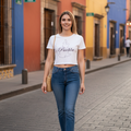 A woman wearing a white short-sleeved crop t-shirt with the text 'Puebla' printed on the front, paired with blue jeans.