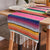Pink rainbow striped table runner with multicolor bands and white fringe ends at both edges.