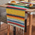 Yellow rainbow striped table runner with green, red, blue bands and white fringe ends.