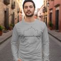 A man wearing a light gray long-sleeve t-shirt with a black outline map of the Aguascalientes state and the text 'Aguascalientes' across the chest, standing in a cobblestone street.