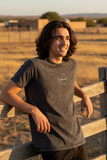 A person wearing a black denim t-shirt with a round neckline and ribbed sleeve cuffs.
