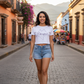 A woman wearing a white crop t-shirt with 'Chiapas' text in black script on the front, paired with blue jeans.