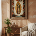 A framed religious art print of Our Lady of Guadalupe hanging on a textured peach wall above a wooden console table, with a cream armchair and throw blanket in the foreground.