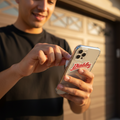 A man in a black t-shirt holding a silver smartphone with a red 'Diablos' logo on the back, standing in front of a garage door.