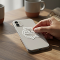 Hand applying a die-cut bubble-free sticker with the word “Morelos” in cursive onto a silver smartphone — featuring a white decorative border and elegant design, symbolizing Mexican regional pride and craftsmanship.