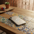 Silver smartphone resting on a wooden table with colorful Mexican ceramic tiles, featuring a die-cut bubble-free sticker shaped like the state of Querétaro — white outline and cursive “Querétaro” text, surrounded by warm lighting, a terracotta pot with a succulent, and rustic décor that evoke artisanal charm and regional pride.