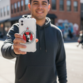 Smiling man outdoors holding a smartphone with a clear case featuring a die-cut bubble-free sticker of the Club Tijuana Xoloitzcuintles de Caliente logo — a red and black circular design with a Xolo dog head and star, representing the Mexican soccer team.