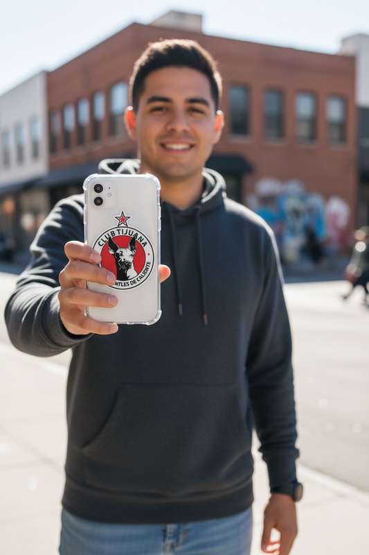 Smiling man outdoors holding a smartphone with a clear case featuring a die-cut bubble-free sticker of the Club Tijuana Xoloitzcuintles de Caliente logo — a red and black circular design with a Xolo dog head and star, representing the Mexican soccer team.