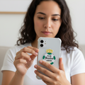  Woman indoors holding a smartphone with a clear case featuring a die-cut bubble-free sticker of the Club Santos Laguna logo — a white and green shield with a gold crown and text “Club Santos Laguna,” representing the Mexican football team.