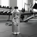 Clear water bottle with a Zacatecas outline sticker and cursive logo placed on a gym floor with weights in the background.