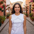 A woman stands on a cobblestone street wearing a white sleeveless tank top with a black outline map of the state of Quinto de Mayo and the text 'Iguasaliente' printed across the chest.