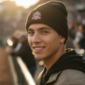 A smiling man in a black Algodoneros de Union Laguna beanie with a 'Tucson, Arizona' logo and a dark jacket, photographed outdoors in warm golden hour light with a blurred stadium background.