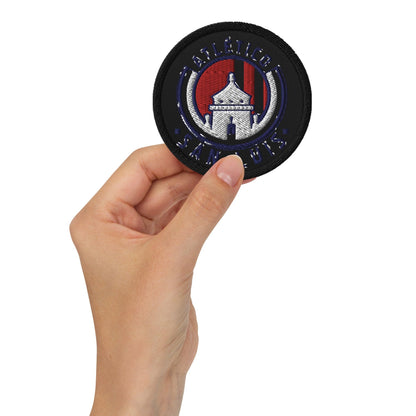 A hand holding a black round embroidered patch with a Club Atletico logo.