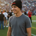 A smiling man on a sports field wearing a black knit beanie with red script lettering Diablos and a gray t-shirt, with a blurred stadium crowd in the background.