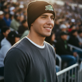 A smiling man in a stadium wearing a black beanie with a green and white 'Pericos de Puebla' logo and a dark gray long-sleeve shirt.