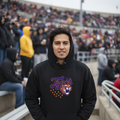A man wearing a black hoodie with a purple and orange 'Tigers' tiger graphic on the chest, standing in an outdoor stadium with a crowd in the background.