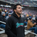 A man wearing a black hoodie with a teal and red 'Bravos' graphic stands in a crowded stadium crowd.
