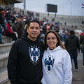 A man and a woman standing together in a stadium, both wearing hoodies with the same blue and white shield logo. The man wears a black hoodie, and the woman wears a white hoodie.