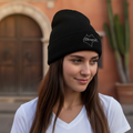 A person wearing a black beanie hat with an embroidered design on the front.