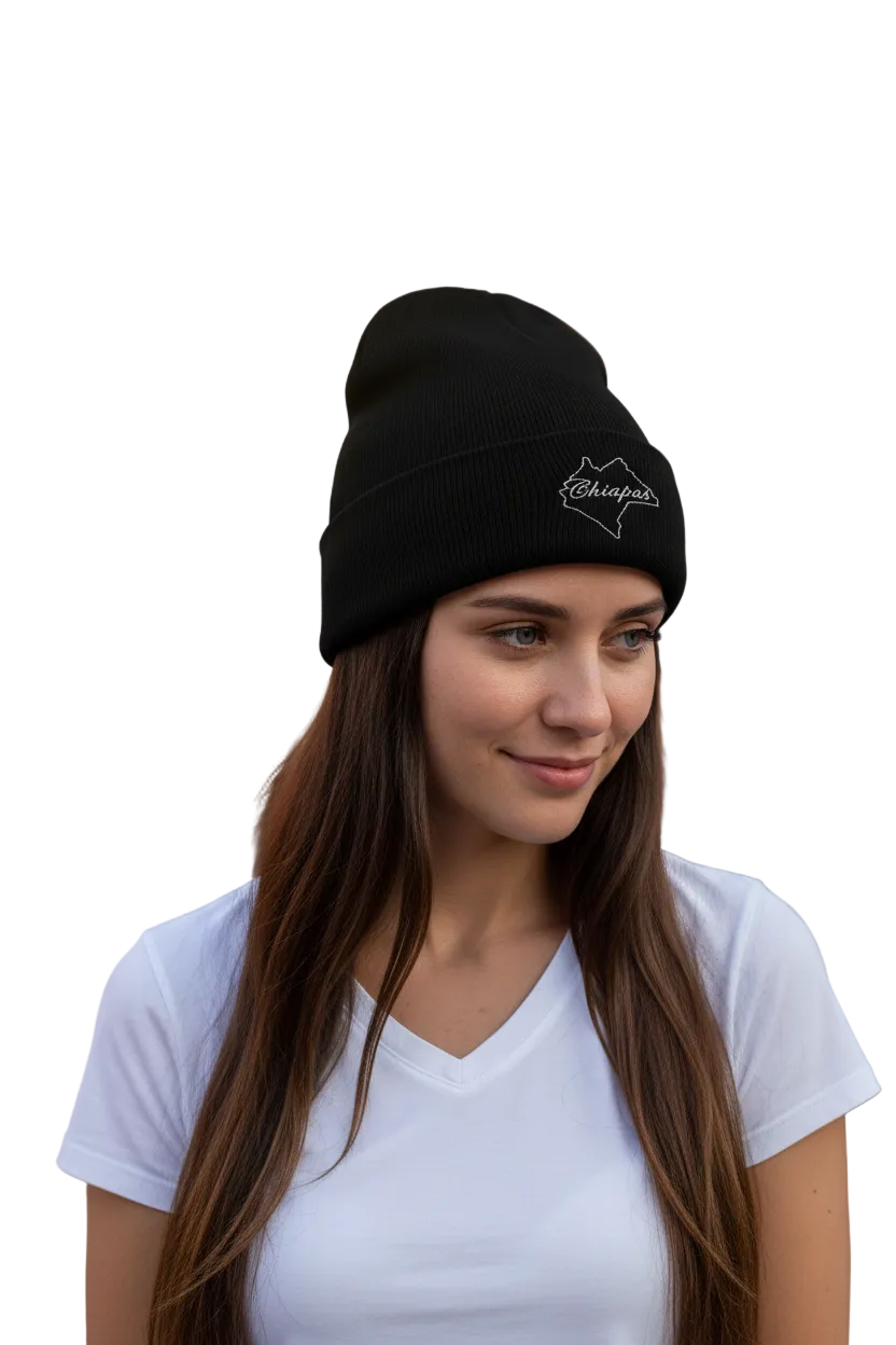 A woman with long brown hair wearing a black knit beanie with a white embroidered mountain logo and the word 'Chiapas' on the front, paired with a white v-neck t-shirt against a solid white background.