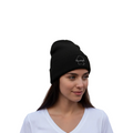 A woman wearing a black knit beanie with a small white embroidered logo on the front, paired with a white V-neck t-shirt, set against a plain white background.