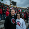 A man and a woman standing together in a stadium crowd, both wearing matching black and white Deportivo Toluca FC hoodies with the club's circular logo on the chest.