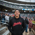 A smiling man wearing a black hoodie with 'Diablos' in red script across the chest, standing in a stadium with spectators in the background.