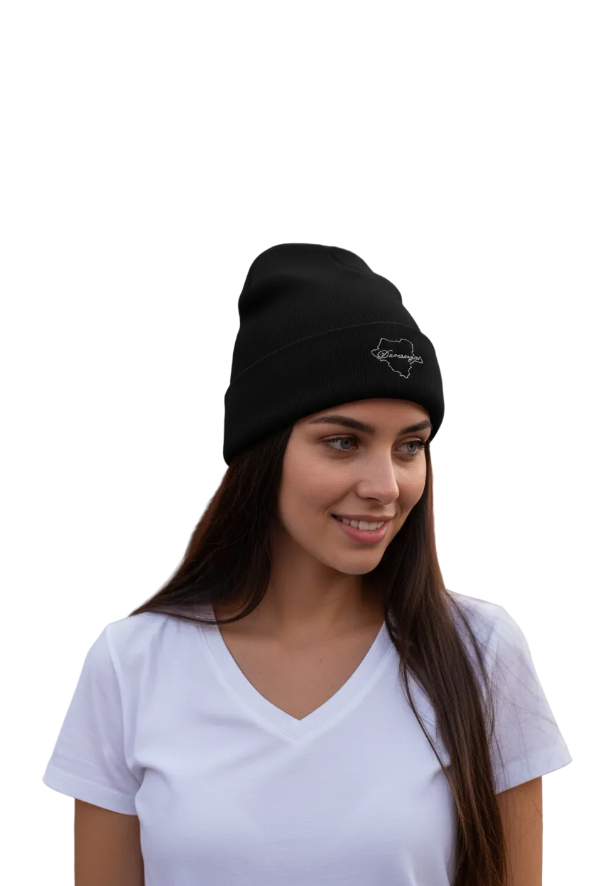 A woman with long dark hair wearing a black Durango knit beanie with a small white embroidered logo on the side, paired with a white V-neck t-shirt, set against a plain white background.
