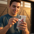 A man in a blue t-shirt holds a white smartphone with a red and black El Aguila de Veracruz logo sticker on the back, standing in front of a garage door.