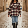 A woman walking down a cobblestone street wearing a long-sleeve plaid button-up shirt in red, black, and beige, paired with light blue jeans and black rain boots.
